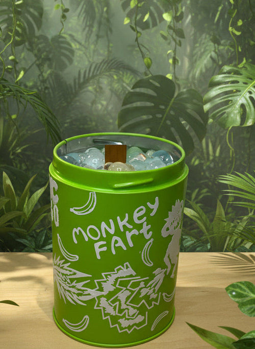Green canister CANDLE labeled 'Monkey Fart' with 3D PRINTED BUBLES on a table with a jungle background